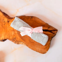 Cargar imagen en el visor de la galería, Pañito facial orgánico enrollado y atado con cinta decorativa en rosado claro, ideal para cuidado personal y regalos.
