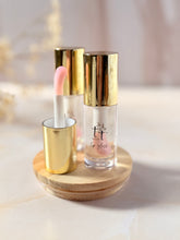 Cargar imagen en el visor de la galería, Lip Gloss Efecto Mágico de Tt atelier con tapa dorada y aplicador rosado, sobre base de madera. Brillo labial artesanal con efecto pH reactivo.