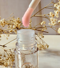 Cargar imagen en el visor de la galería, Aplicador del ip Gloss Efecto Mágico de Tt atelier, saliendo del frasco, rodeado de flores secas doradas. Brillo labial artesanal con efecto pH.