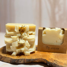 Cargar imagen en el visor de la galería, Jabón artesanal con topping cremoso y flores secas, presentado en base de madera junto a empaque natural de Tt atelier.