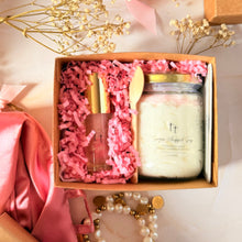 Cargar imagen en el visor de la galería, Caja de regalo artesanal abierta con scrub corporal, lip gloss y cucharita de madera, acompañada de accesorios decorativos.