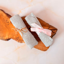 Cargar imagen en el visor de la galería, Textura en primer plano: dos toallitas faciales color gris, enrolladas y atadas con lazos, sobre una madera.
