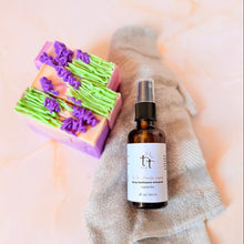 Cargar imagen en el visor de la galería, Spray sanitizante artesanal Manitas Limpias con aroma a lavanda, junto a tres barras de jabones de Lavanda y una toalla gris sobre un fondo claro. Producto de Tt atelier.