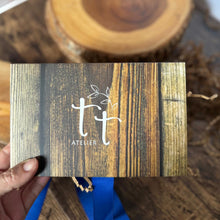 Cargar imagen en el visor de la galería, Caja de regalo artesanal cerrada con diseño de vetas de madera y logo de Tt atelier al frente.
