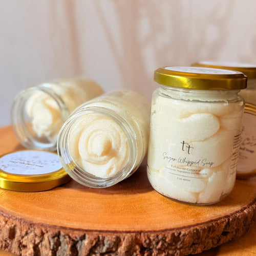 Frascos de Sugar Whipped Classic Coco, sobre base de madera rústica, un frasco abierto muestra la textura del exfoliante.