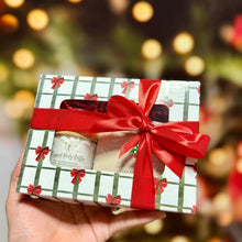 Cargar imagen en el visor de la galería, Caja navideña artesanal con ventana y lazo rojo, con productos de Tt atelier en su interior.
