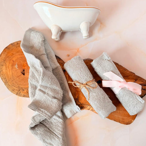 Tres toallitas faciales orgánicas sobre fondo de madera: una semi abierta mostrando su suave textura, otra enrollada con cinta de yute y una mas con lazo rosado.
