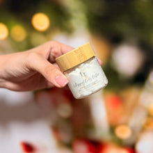 Cargar imagen en el visor de la galería, Frasco de whipped body butter edición navideña, sostenido en mano frente a luces festivas.
