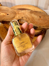 Cargar imagen en el visor de la galería, Frasco de aceite corporal iluminador Lumière Gold sostenido en la mano, mostrando su tamaño práctico y el brillo dorado del producto
