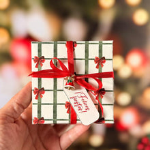 Cargar imagen en el visor de la galería, Caja navideña pequeña sostenida en la mano, con lazo rojo y pin decorativo.
