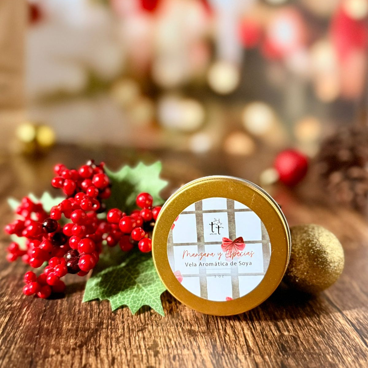 Vela aromática de soya en lata dorada con etiqueta navideña de Tt atelier, ambientada con ramas rojas y decoración de Navidad.