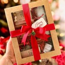 Cargar imagen en el visor de la galería, Caja de regalo artesanal de Tt atelier, decorada con un lazo rojo y un pin navideño dorado. En el interior se ven jabones y productos envueltos en papel kraft, presentada sobre un fondo cálido y festivo.
